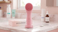 Cepillo facial sónico rosa mojado sobre lavamanos de mármol junto a productos de skincare