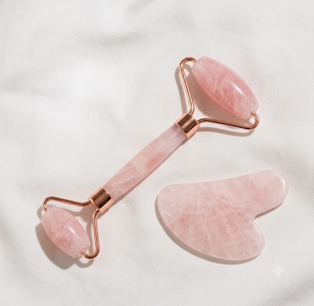 Rodillo facial y piedra gua sha de cuarzo rosa sobre tela blanca, vista de detalle
